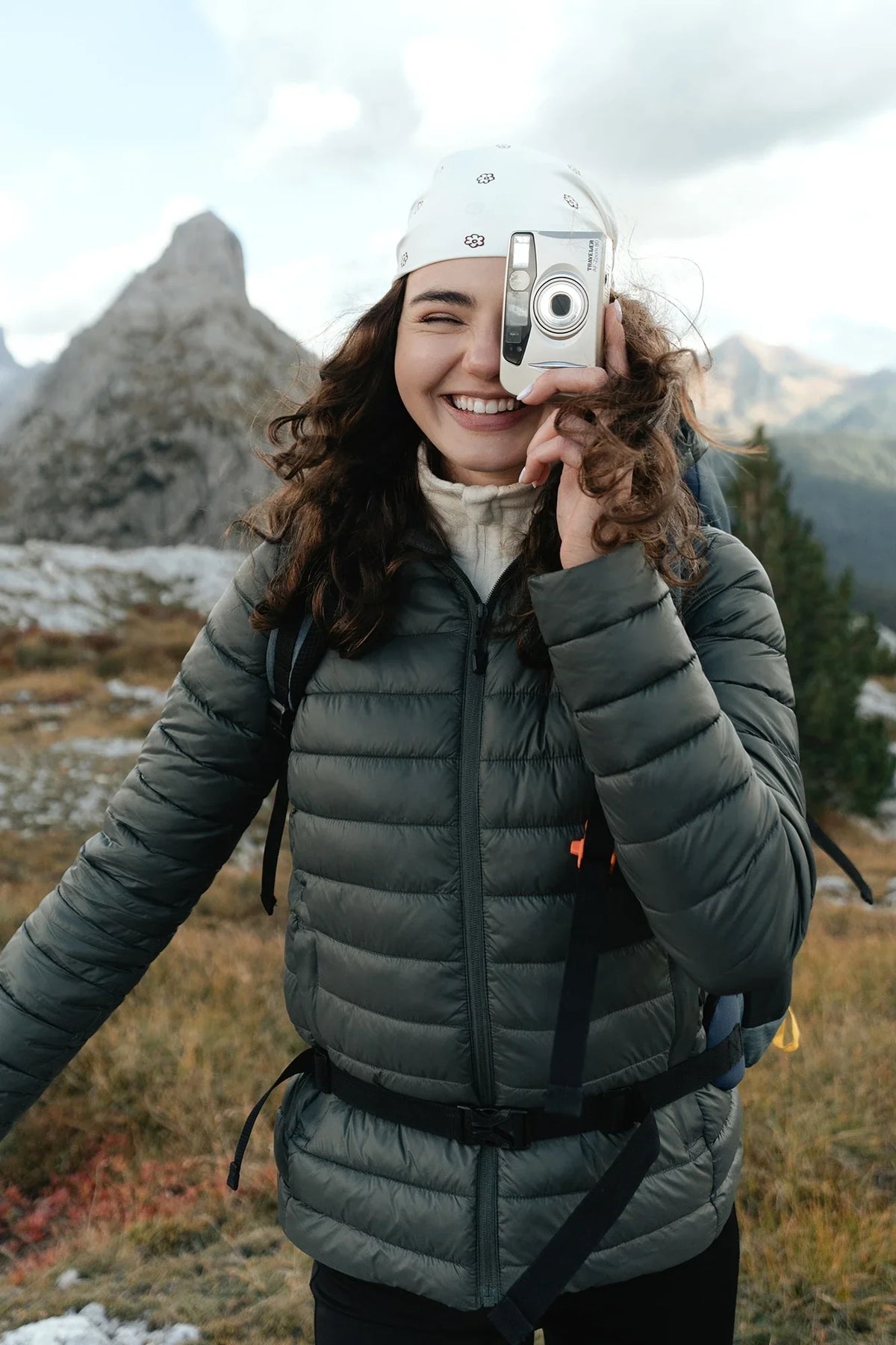Woman in a dark green quilted jacket taking photos in the mountains