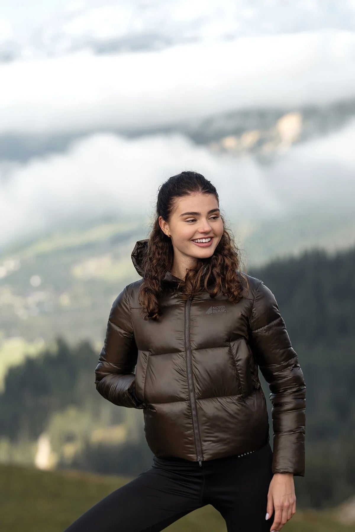 Woman in a brown winter jacket in the mountains above the clouds