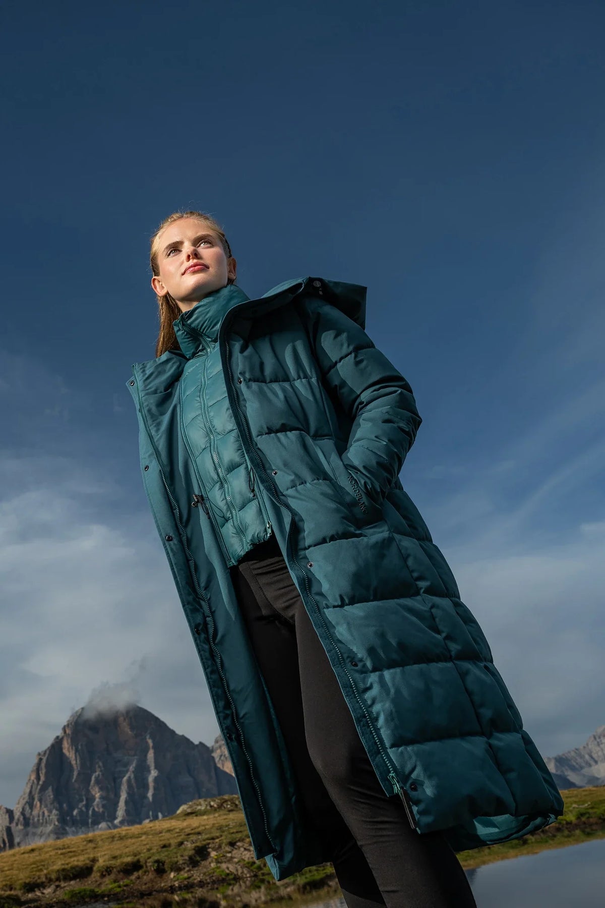 Woman in a long petrol-coloured winter coat in the mountains